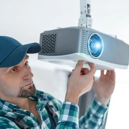 A technician adjusting a ceiling-mounted projector with the lens illuminated.