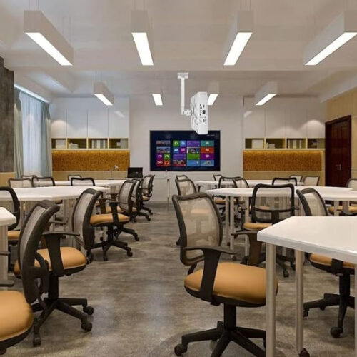 Classroom with a ceiling-mounted projector, multiple desks, and ergonomic chairs.