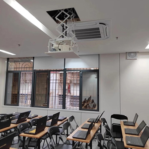 Classroom with ceiling-mounted projector and rows of desks with laptops.