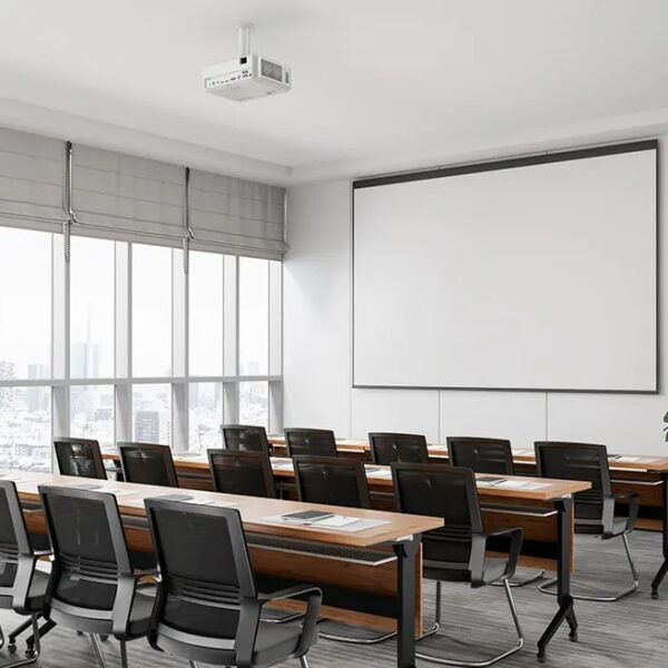 Bright training room with rows of desks, black chairs, and a ceiling-mounted projector.