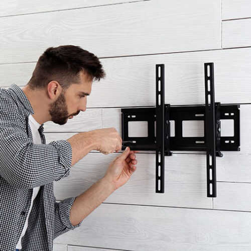 A man installing a black TV wall mount on a white wooden wall.