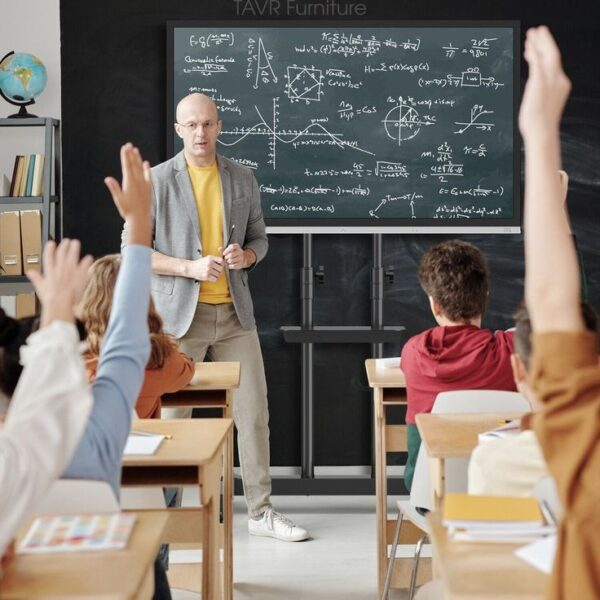 Teacher explaining math on a large screen in a classroom.